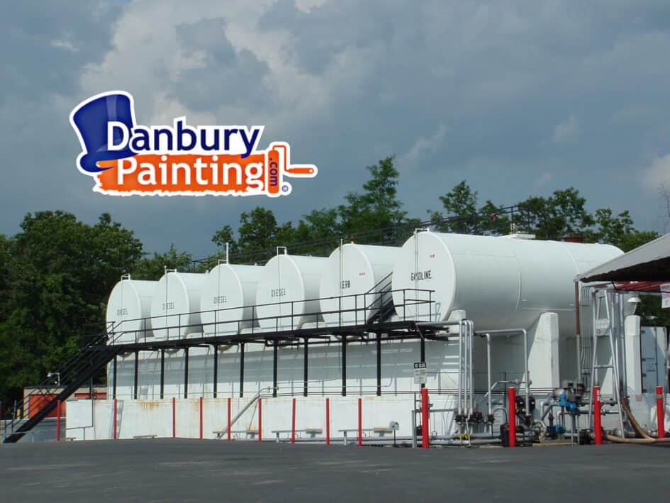 Industrial fuel storage yard with white diesel tanks and a large Danbury Painting logo in the sky.